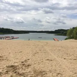 Plaża nad jeziorem Niedzięgiel, z pomostami i łódkami, w tle las.