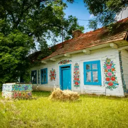 Kolorowy dom z malowanymi kwiatami, niebieskimi oknami i drzwiami. Idealne miejsce na trasie do Zalipia.