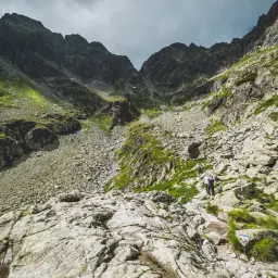 Kamienista ścieżka w górach, gdzie widać ludzi idących w kierunku szczytu. Widok zapiera dech, a krajobraz wywołuje zawrót głowy.
