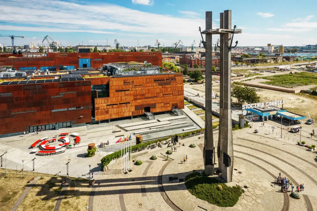 Monument upamiętniający robotników Stoczni Gdańskiej. W tle nowoczesne budynki i historyczne dźwigi. Sprawdź cennik zwiedzania!